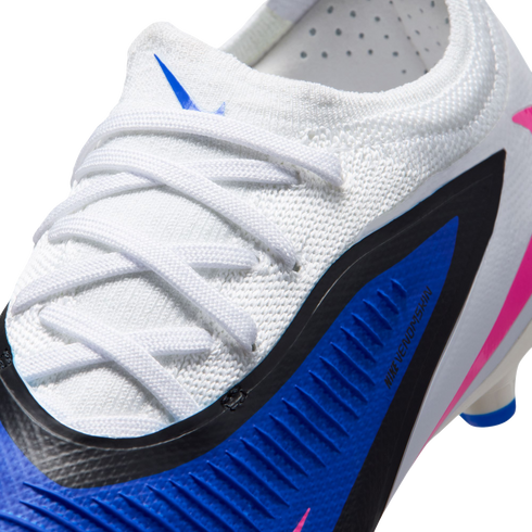 Close-up of a white Nike soccer cleat featuring a blue and black panel with "NIKE VENOMSKIN" branding, white laces, and pink accents.