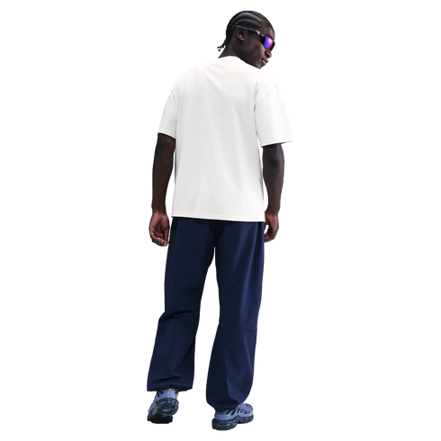 Rear view of a person with braids wearing a white T-shirt, navy baggy pants, and blue sneakers against a solid black background.