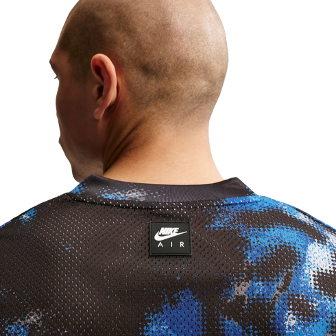 Close-up of the back of a bald man in a black and blue mesh Nike Air jersey with a small logo on the center back.