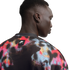 A close-up, back-profile view of a person wearing a black mesh Nike Air shirt with a vibrant red, blue, and pink abstract paint-splatter pattern.