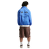 Back view of a person wearing a blue "AIR" windbreaker jacket, brown cargo shorts, and sneakers.