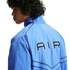 A person with curly dark hair seen from behind, wearing a light blue zip-up jacket with "AIR" printed in black on the back and black piping details.