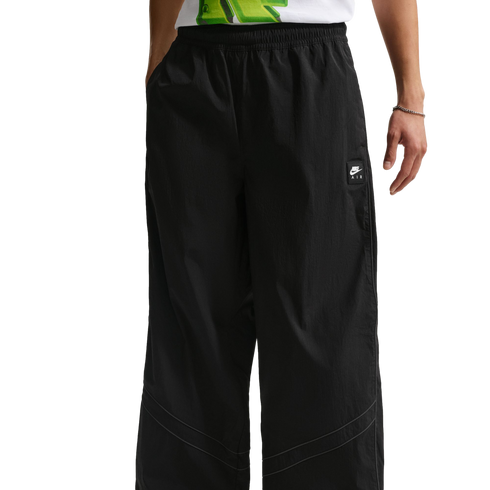 A person wears black wide-leg Nike Air trousers with thin grey curved piping around the knees.