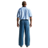 Back view of a man wearing a light blue patterned short-sleeve shirt and wide-leg denim jeans against a white background.