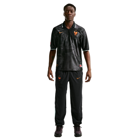 Full-length photo of a man in a black Nike France training kit with orange details, standing against a white background.