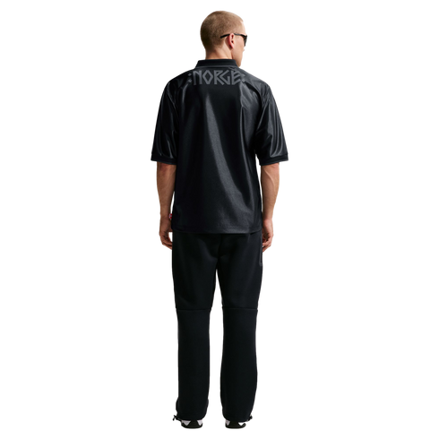 Back view of a man wearing a black jersey with "NORGE" across the upper back and black sweatpants, standing against a white background.