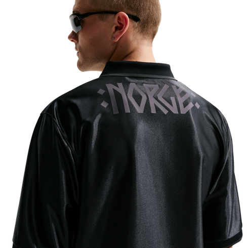 Back view of a man in a black shiny jersey with "NORGE" in grey stylized letters across the shoulders. He wears sunglasses and looks left against a white background.