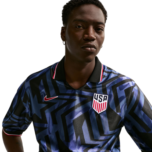 A man wearing a blue and black geometric pattern Nike USA soccer jersey with a USA crest, against a plain white background.