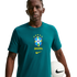 A young man wearing a teal Nike t-shirt with the Brazil national soccer team crest, holding a white soccer ball against a solid black background.