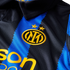 Close-up of an Inter Milan jersey with blue and black jagged stripes. It features the team's gold crest under two stars and part of a yellow sponsor logo.