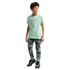 A young boy stands against a solid black background. He is wearing a light mint green short-sleeved T-shirt with the word "FRANCE" and a Nike swoosh in gold, patterned camouflage joggers, and black sneakers.