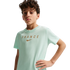 A young boy with curly brown hair wearing a light mint green t-shirt with "FRANCE" and a Nike swoosh printed in gold across the chest. He stands with one hand on his hip against a solid black background.