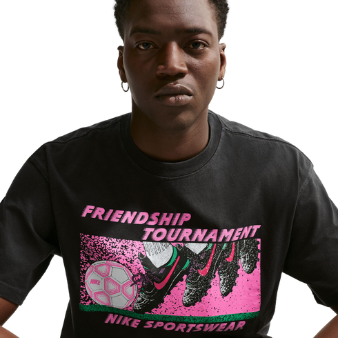A person wearing a black Nike t-shirt with a pink and green "FRIENDSHIP TOURNAMENT" soccer graphic on the front.