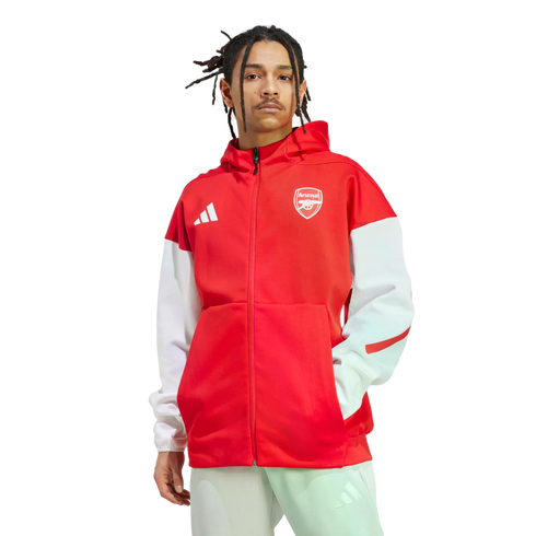 A man with dreadlocks wearing a red and white Adidas Arsenal zip-up hoodie and light-colored pants, posed against a white background.