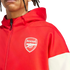 A person with dreadlocks wearing a red zip-up hoodie featuring the Arsenal football club crest on the chest and white color-block sleeves.