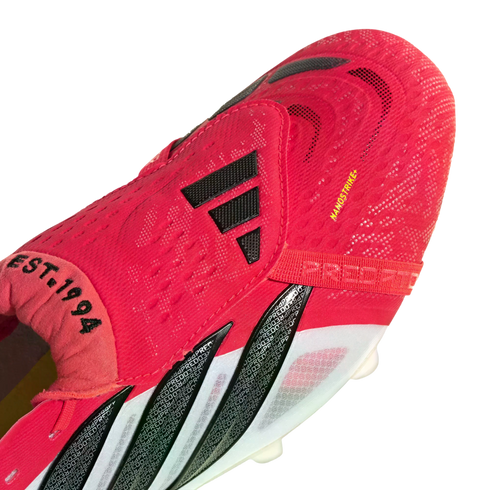 Close-up of a red Adidas Predator soccer cleat with black stripes, white side accents, and the text "EST. 1994" and "NANOSTRIKE+".