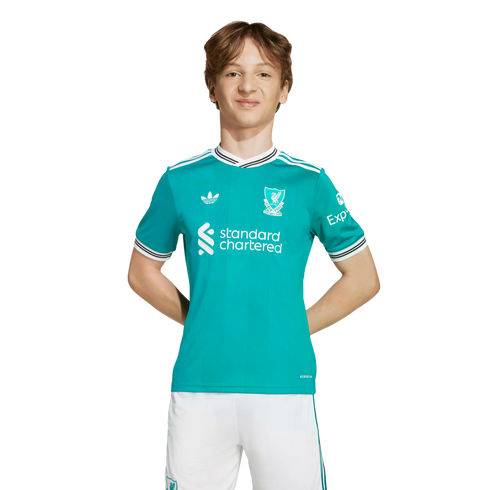 A young person with wavy brown hair wearing a teal Liverpool FC soccer jersey and white shorts, standing against a solid black background.