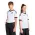 Two youths wearing white Mexico national team soccer jerseys with green and red trim and black pants, standing against a solid black background.