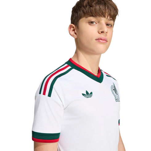 A young man wearing a white Mexico football jersey with green and red trim, an Adidas logo, and team crest, set against a black background.