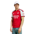 A man poses in a red and white Arsenal football jersey, light blue jeans, and a white baseball cap against a white background.