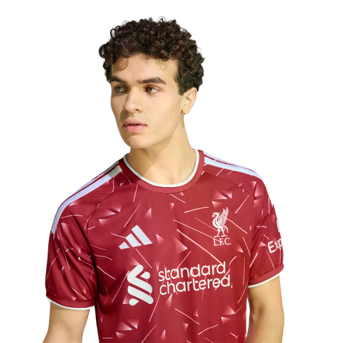 Man with curly brown hair wearing a red Liverpool FC soccer jersey, looking to the side against a plain white background.