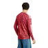 Rear view of a man wearing a red patterned long-sleeve jersey with white stripes and blue denim jeans against a white background.