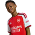 A smiling young Black boy wearing a red and white Arsenal football jersey against a white background.