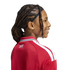 Profile of a smiling child with dark hair in twists, wearing a red and white "UNITED" athletic jacket against a white background.
