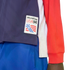 A close-up of a navy blue, white, and red athletic top featuring an official "WorldCup USA94" patch on the bottom left side. The patch includes the event's logo with a soccer ball and red stripes. The person is also wearing bright blue shorts.