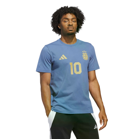 Man with curly hair wearing a light blue Argentina t-shirt with a gold number 10, posing against a solid black background.