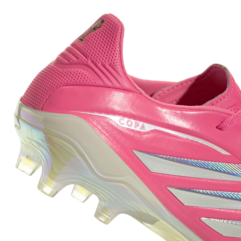 Close-up of the heel of a pink soccer cleat featuring silver "COPA" branding, silver stripes, and an iridescent translucent soleplate with studs.
