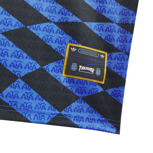 Close-up of a blue and black diamond-patterned fabric with repeated AFA logos and a yellow-bordered Thrasher and Argentine Football Association patch.