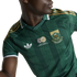 A person wearing a green South Africa national football jersey with gold shoulder stripes, a white Adidas logo, and the national team crest over a patterned fabric.
