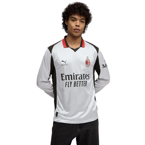 Man in a white AC Milan long-sleeve soccer jersey with red and black accents and 'Emirates Fly Better' logo, against a black background.