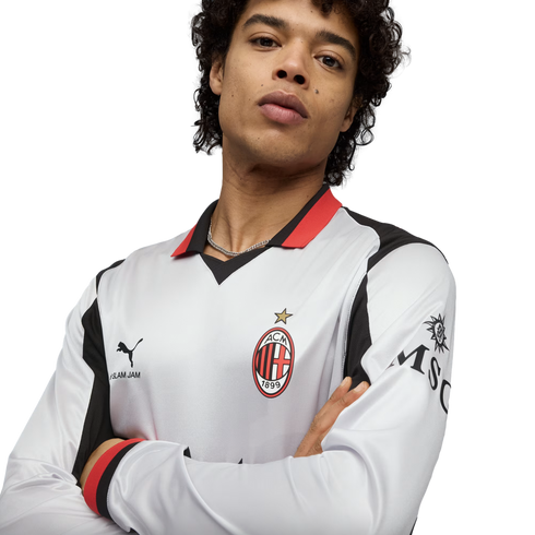 A man wearing a white AC Milan long-sleeve jersey with red and black accents, posing with arms crossed against a black background.