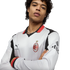A man wearing a white AC Milan long-sleeve jersey with red and black accents, posing with arms crossed against a black background.