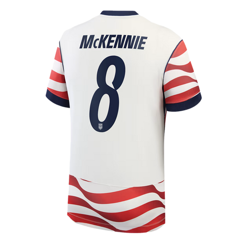A studio product shot showing the back of a white US Men's National Team soccer jersey. The name "MCKENNIE" and the number "8" are printed in dark blue on the back. Wavy red and white horizontal stripes decorate the sleeves and the bottom hem of the shirt