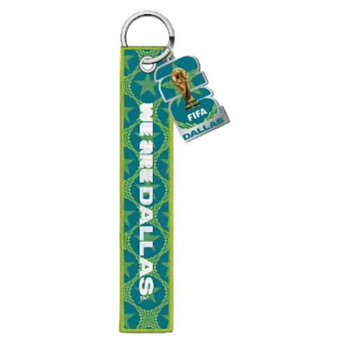 Teal and lime green FIFA World Cup Dallas keychain. A long fabric strap features a geometric star pattern and vertical white text reading "WE ARE DALLAS." An attached shaped charm depicts the World Cup trophy and the words "FIFA DALLAS."