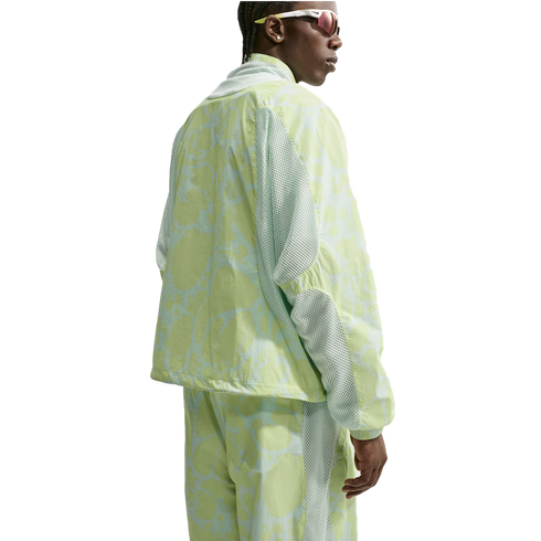 A person wearing a lime green and light blue abstract patterned tracksuit with mesh panels and sporty sunglasses, seen from the back against a white background.