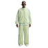 A person wearing a light green and white patterned Nike tracksuit, futuristic white sunglasses, and white sneakers against a white background.