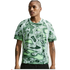 A man wearing a green and white abstract-patterned t-shirt with raglan sleeves and black shorts against a white background.