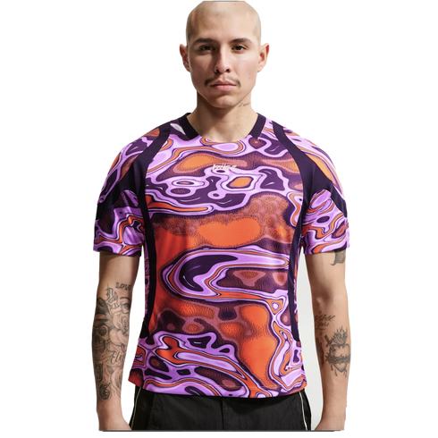 A bald man with arm tattoos wearing a vibrant purple and orange swirl-patterned athletic shirt.